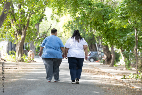 Obesity Concept- Indian couple walking together at summer park to loose weight. Plus size friends Fitness and healthy lifestyle. Fat man and woman outdoor. Back view.