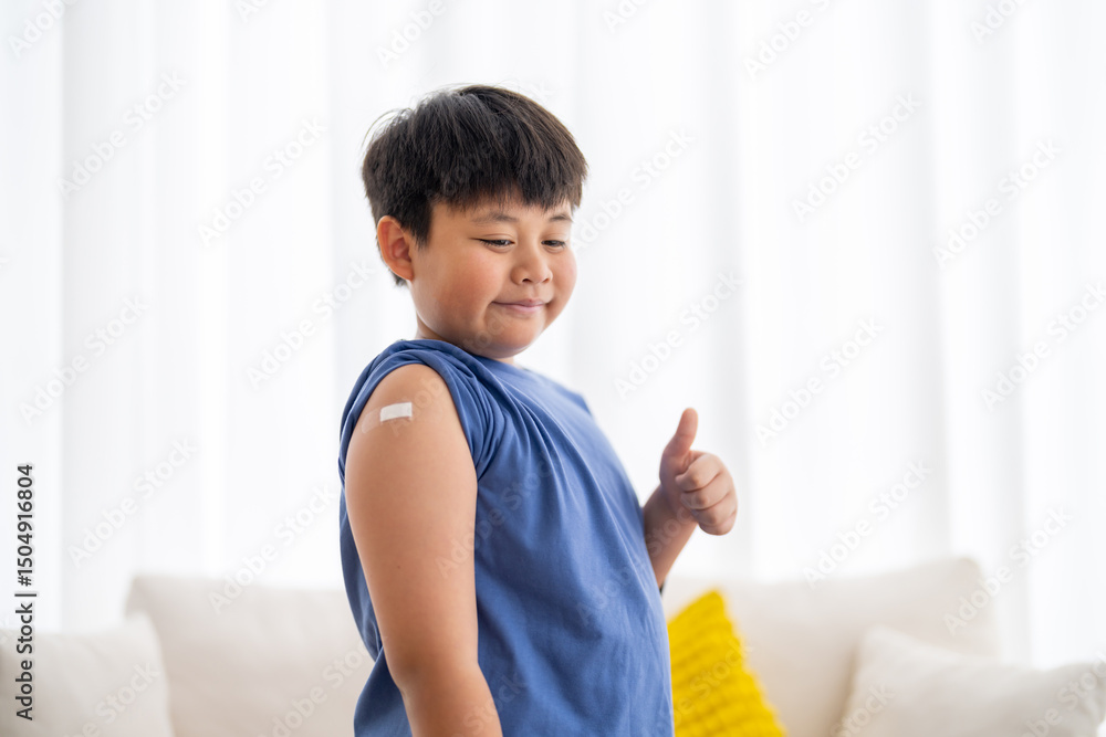 Asian boy giving thumbs up after vaccination shows confident with bandage on arm, child health care, hospital service, influenza vaccine protection, covid prevention, pediatric safety immunity booster Asian boy giving thumbs up after vaccination shows confident with bandage on arm, child health care, hospital service, influenza vaccine protection, covid prevention, pediatric safety immunity booster