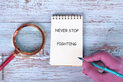 The concept of inspirational and motivational. NEVER STOP FIGHTING on a handwritten note placed next to a magnifying glass on old boards