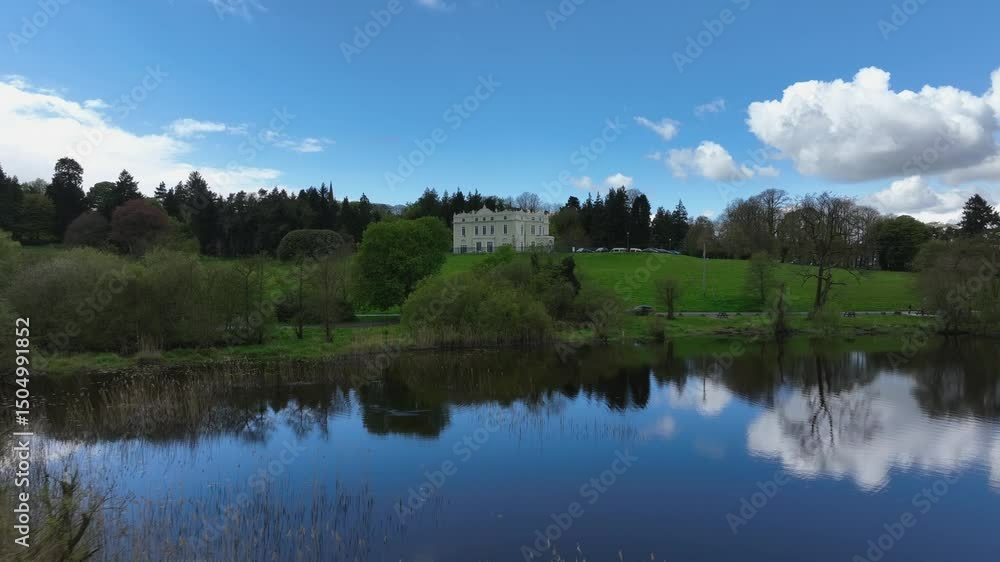 Hope Castle, County Monaghan, Ireland, September 2022. Drone low approach over tall reeds along lake shore of Lough Muckno establishing building centered above grassy lawn under blue sky. Hope Castle, County Monaghan, Ireland, September 2022. Drone low approach over tall reeds along lake shore of Lough Muckno establishing building centered above grassy lawn under blue sky.