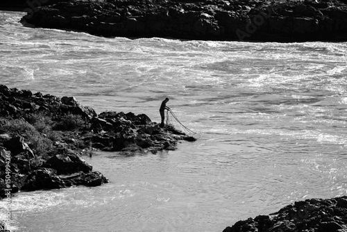 Black and white photo of a man fishing by the river in Iceland