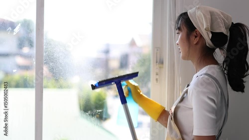 Wallpaper Mural Asian housekeeper wearing an apron and rubber gloves is spraying and cleaning a glass window using a spray bottle and a squeegee. Torontodigital.ca
