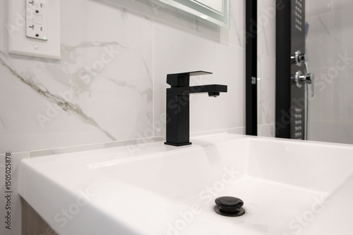 фотографія Modern black faucet on a clean white sink in a bathroom with marble tile