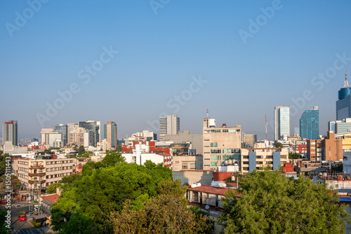 Elevated view of Mexico City skyline with modern and traditional buildings, trees, and clear sky, ideal for business, architecture, real estate and urban development stock.