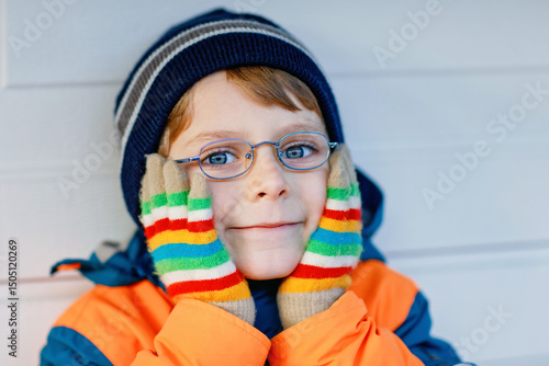 Portrait of little cute school kid boy with glasses and colorful winter fashion clothes. Child smiling and having fun with the camera. Winter, spring or autumn fashion. Kid with missing front teeth