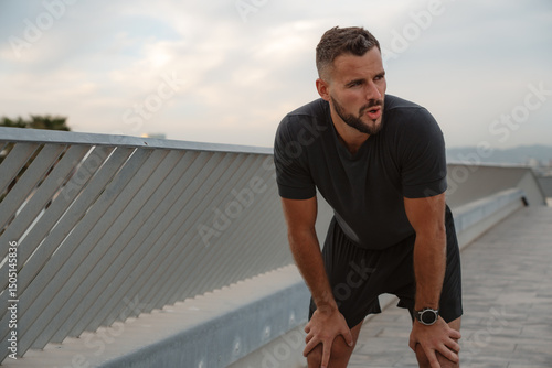 Carta da parati Exhausted male athlete resting on a bridge, catching his breath after an intense
