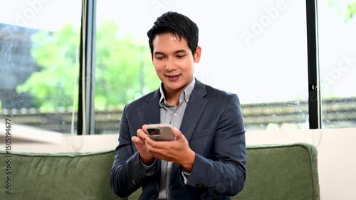Asian businessman in suit using laptop during remote work meeting. Smiling and confident in modern office