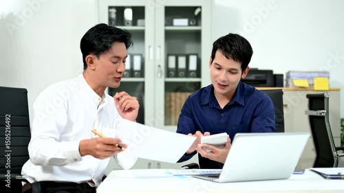 Two Asian businessmen working together at a desk, analyzing charts and discussing project strategy. , and teamwork.
