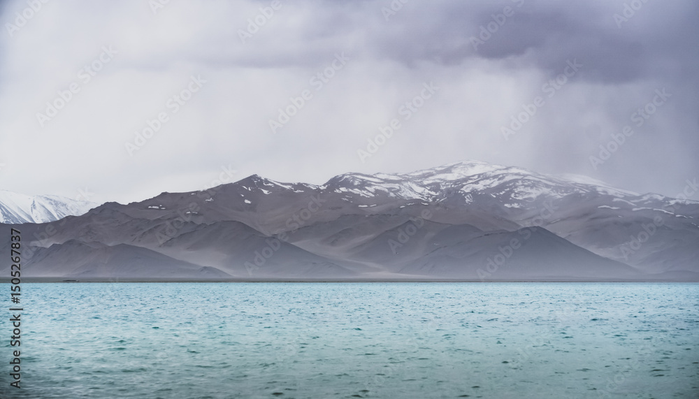 Lake Karakul with blue water and mountain peaks in the background, cloudy weather and sky with clouds and clouds, rainy highland landscape in the Pamirs Lake Karakul with blue water and mountain peaks in the background, cloudy weather and sky with clouds and clouds, rainy highland landscape in the Pamirs