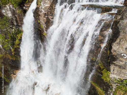 Mesmerizing drone view of a majestic Norwegian waterfall cascading down rocky ledges amidst wild nature.