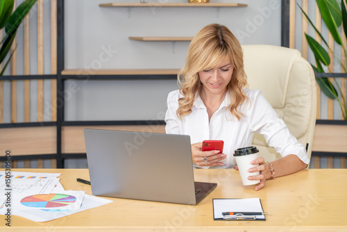 Focused Businesswoman Working on Laptop, Holding Coffee and Phone. Copy space.