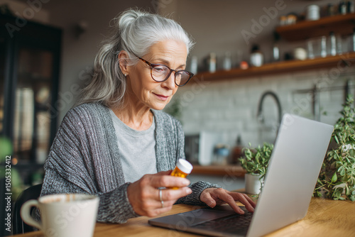 Senior woman using laptop computer to research medication refills online from home kitchen