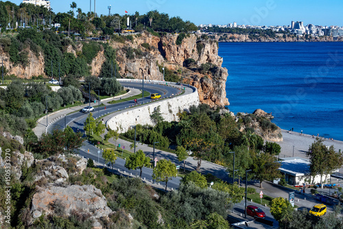 S-shaped winding road descending to Konyaaltı Beach with cars, rocky cliffs and blue sea. Shot from viewpoint. Antalya, Turkey