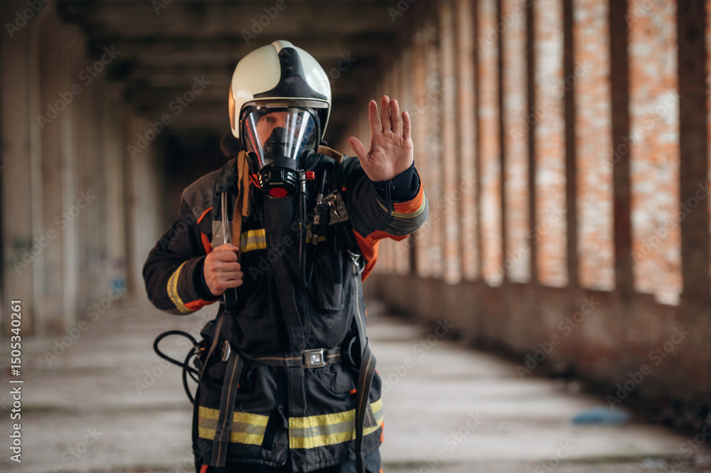 Obraz premium Stop hand gesture. Firefighter in professional equipment is indoors in abandoned building