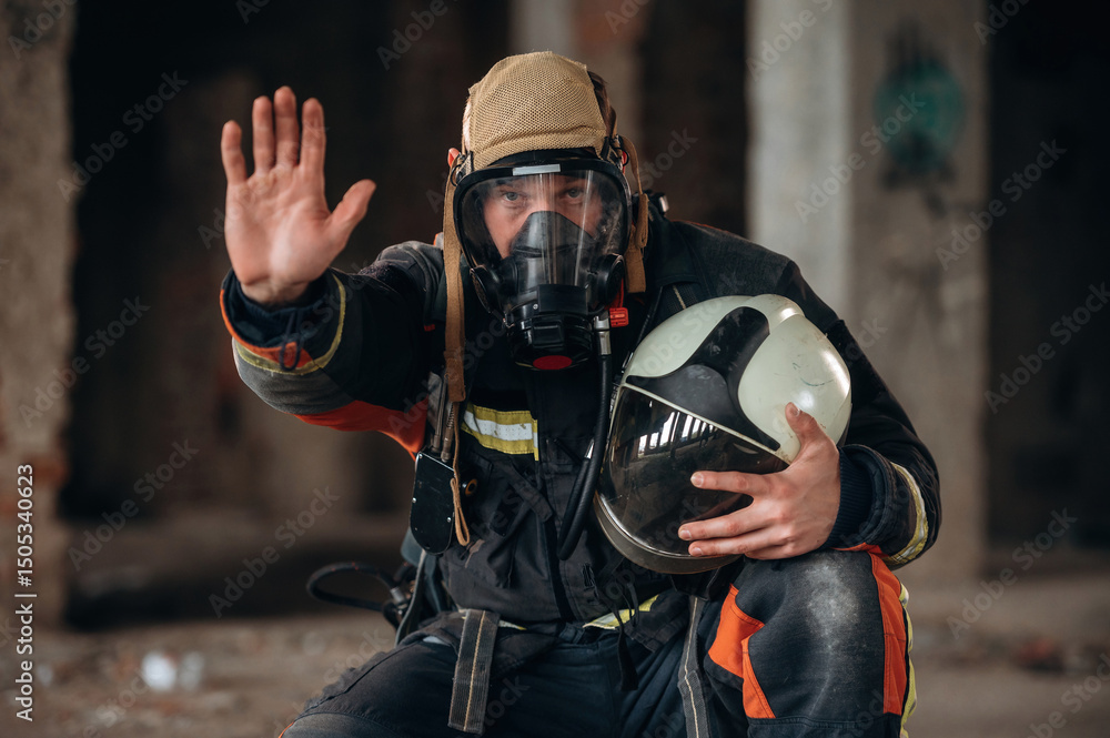 Obraz premium Stop hand gesture. Firefighter in professional equipment is indoors in abandoned building