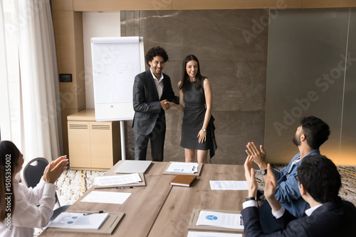 Glad to welcome in team. Happy smiling professional male boss leader introduce young female newcomer to diverse international department workforce handshaking new employee on staff boardroom meeting