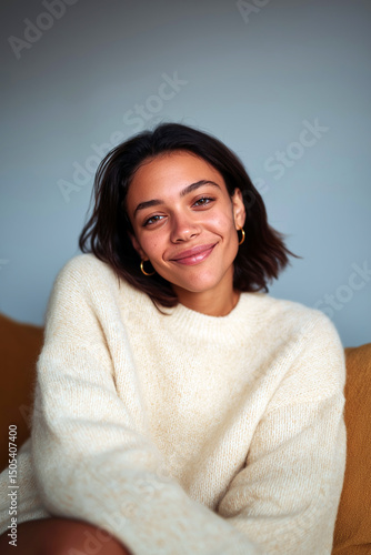 Young woman smiling warmly in cozy white sweater sitting on sofa in relaxed indoor atmosphere