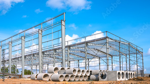 Metal structure of industry warehouse factory building with concrete drainage pipes on the ground in construction site against blue sky background, perspective side view 