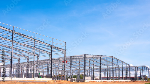 Metal columns and roof beam structure of three industry warehouse factory buildings with workers are working in large construction site against blue sky background, side view