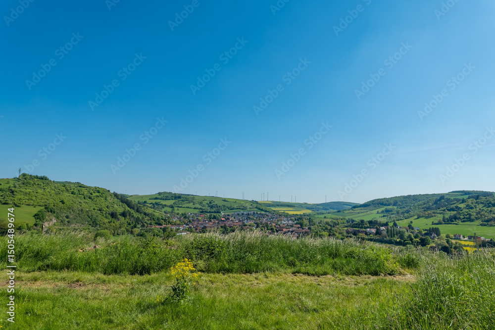 Fototapeta premium Endless green hills embrace a charming village under a bright blue sky on a sunlit day