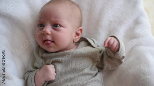 Baby with blue eyes in olive overalls lies on back. Close-up. Child looks around. First year of life and hygiene of child. Newborn - happiness for family. New worries and style life.