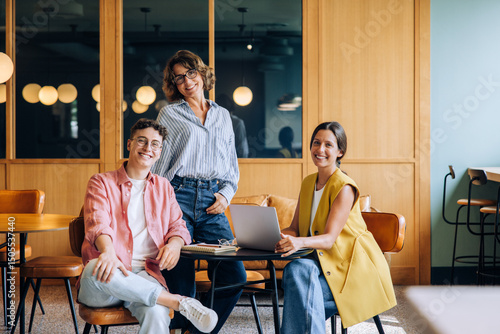 Three colleagues in a casual setting discussing ideas and working on a laptop photo