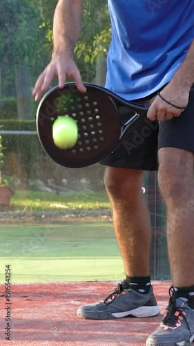 Seville, Spain-28 July, 2021: Vertical, Slow motion a padel player who bounces the ball and serves in a match on an outdoor court.