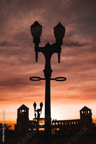 Cuadro en lienzo Sunset photo with the silhouette of a lamppost in the foreground, with a symmetrical building in the background consisting of two towers and a walkway
