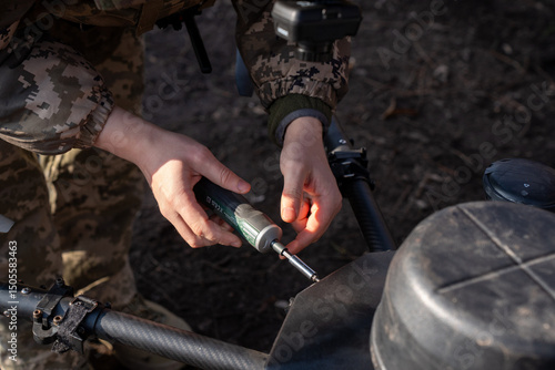 A soldier in camouflage adjusts sensitive equipment in a wooded area. The individual focuses intently on the task, ensuring everything functions properly.