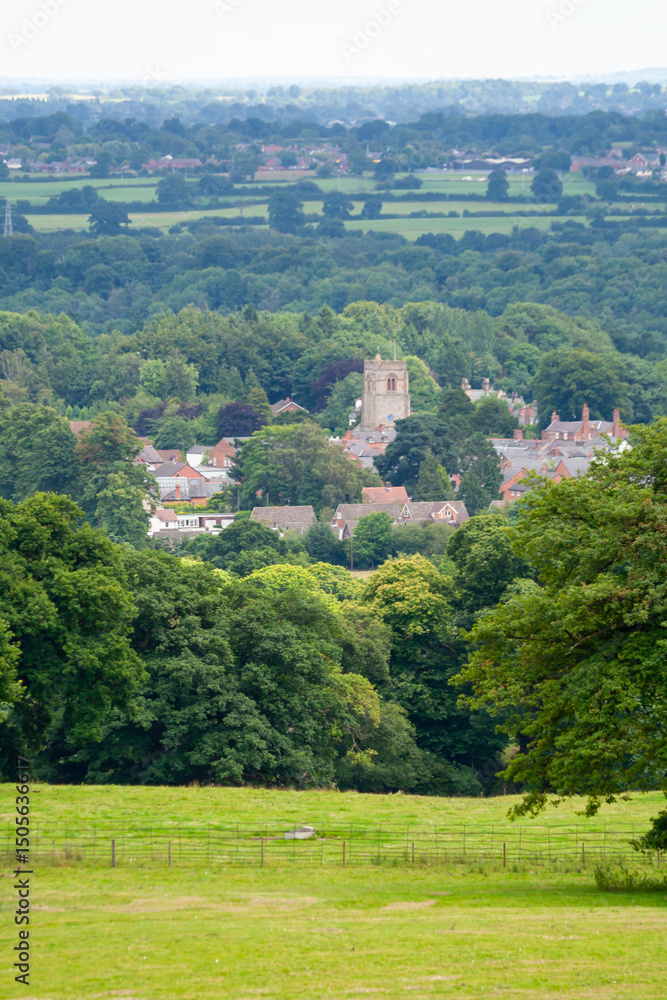 Obraz premium Our green and pleasant land, landscape view over forests towards a village with a church at its centre in rural England on a summers day, nature and space surrounding a lovely place to live.