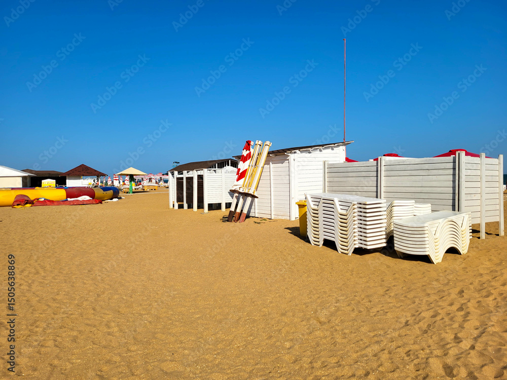 Obraz premium An urban seaside beach with canopies and assembled white deck chairs against a cloudless sky