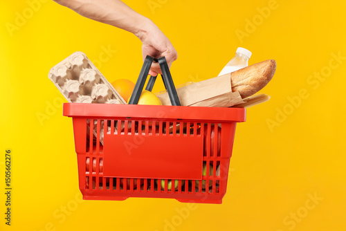 Man holding shopping basket with different products on yellow background, closeup