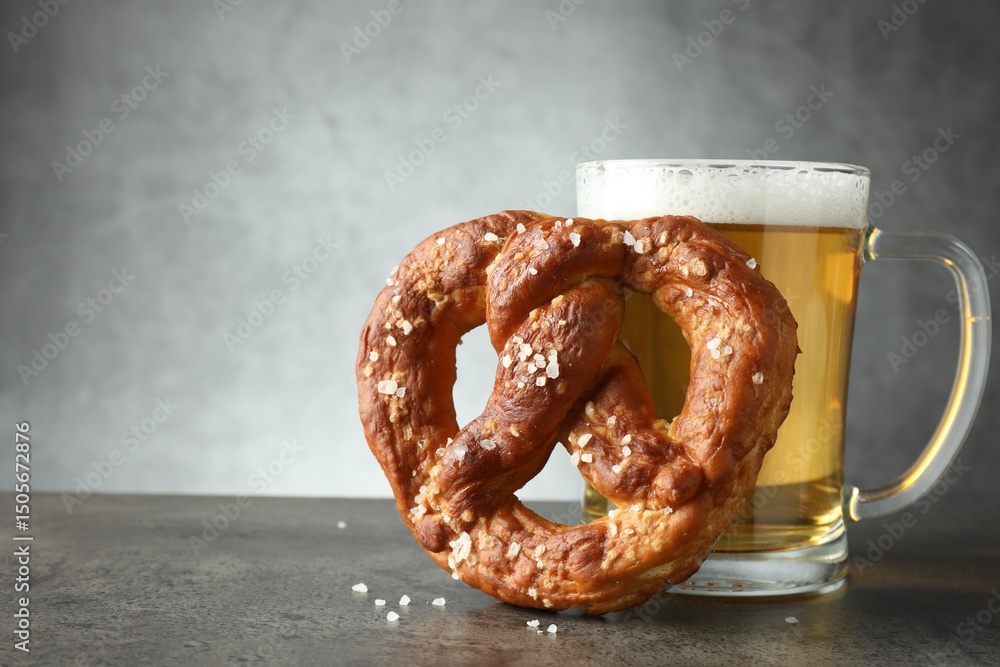 Tasty pretzel and glass of beer on dark textured table against grey background, closeup. Space for text Tasty pretzel and glass of beer on dark textured table against grey background, closeup. Space for text