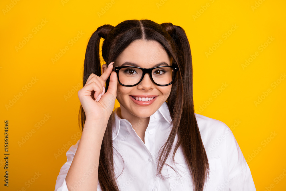 Portrait of a cheerful young woman with glasses and twin ponytails wearing a white shirt against a bright yellow background Portrait of a cheerful young woman with glasses and twin ponytails wearing a white shirt against a bright yellow background