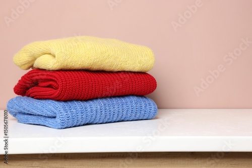 Stack of woolen sweaters on white table against color background. Space for text