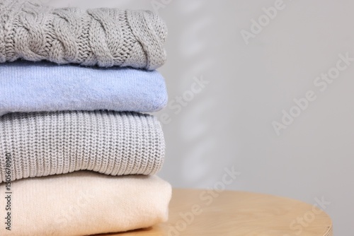 Stack of woolen sweaters on wooden table against light background, closeup. Space for text