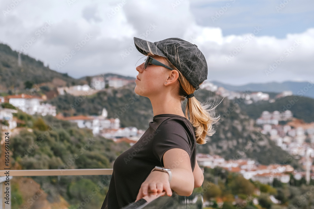 Fototapeta premium Travel,Young female traveler walking alone alongscenic mountain road solo travel, digital nomad lifestyle, eco-friendly road trip adventure.moment of mindful journeyexploration in nature.