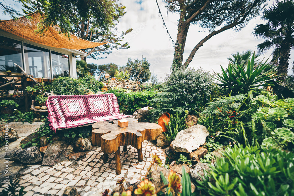 custom made wallpaper toronto digitalCozy outdoor garden seating area with a rustic wooden bench covered in a crochet blanket and a natural tree stump table, surrounded by lush greenery, succulents, and stone paving