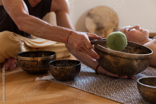 Sound healing ceremony in a yoga studio with Tibetan singing bowls, incense, and meditating participants. Peaceful atmosphere with natural light and warm tones