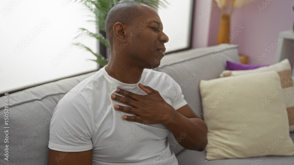 custom made wallpaper toronto digitalYoung man experiencing discomfort sitting on sofa in living room, showing expression of pain, hand on chest, inside modern apartment with cushions and plants.