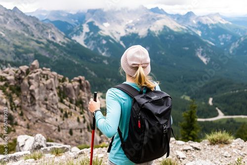 Hiker standing on mountain peak overlooking winding road through majestic mountain range landscape