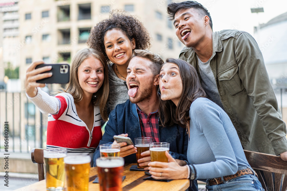 Fototapeta premium Group of diverse young friends making funny faces while taking a selfie and enjoying beers at an outdoor bar. They are laughing and celebrating friendship in a relaxed urban setting. Gen Z concept.