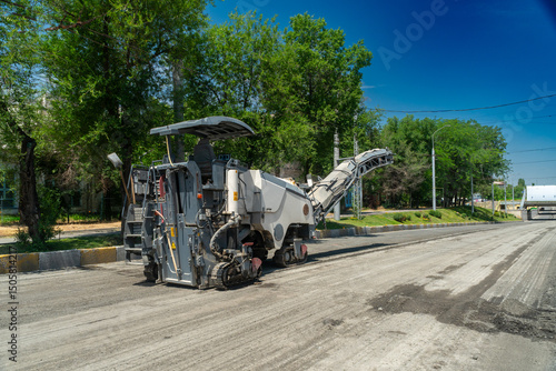 Heavy road milling equipment grinds and removes worn asphalt surface, preparing roadway for new paving. Urban infrastructure, construction process, machinery operation, transportation upgrade