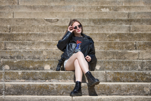 Quadro em tela pretty young blonde woman wearing sunglasses and dressed like a rocker is sitting cross-legged on the steps of a staircase
