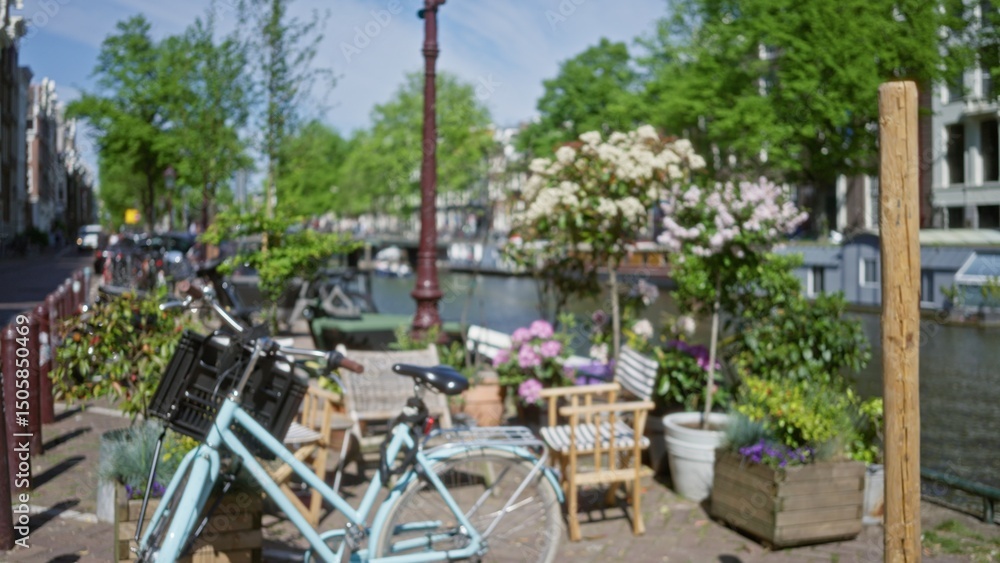 Fototapeta premium Amsterdam scene with blurred bicycle and flowers near canal, showcasing defocused urban setting with greenery and iconic netherlands canal view.