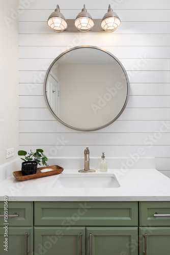 Fotografie A bathroom detail with a green cabinet, white marble countertop, shiplap accent wall, and a light fixture mounted over a circular mirror