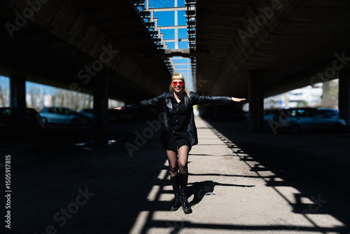 Foto Punk style fashion girl in black edgy outfit with leather jacket and bold red sunglasses, expressing confident alternative street wear attitude in a modern urban setting