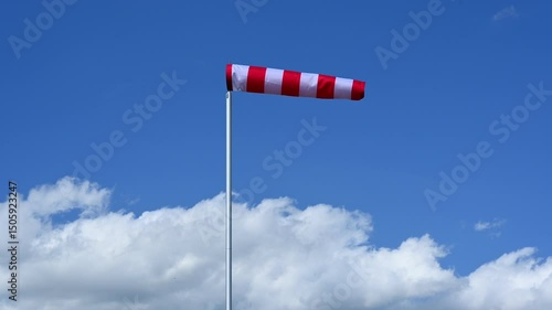 red and white windsock against blue sky and white cumulus clouds