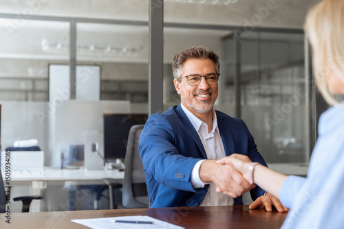 Canvas Print Mature Latino bank worker man shaking hand with client, recruit female employee or business partner after signing a contract