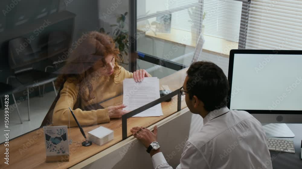 High angle shot of woman with curly red hair getting help with paperwork from bank assistant across counter